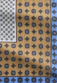 Brązowy i niebieski jedwabny szalik w wzory, z geometrycznymi kształtami w powtarzającym się układzie na teksturowanym tle. Motywy rozmieszczone w równych odstępach.