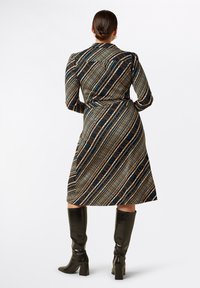 Flerfärgad mönstrad klänning med långa ärmar, figursydd passform, midjeband och knälång nederkant, tillsammans med glänsande svarta stövlar som når upp till knäna.