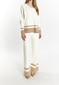V-neck cream sweater with brown stripes at the hem and sleeves, paired with cream wide-leg pants, complemented by beige pointed shoes.
