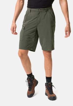 Mann trägt olivegrüne Cargo-Shorts, schwarze Socken und braune Wanderschuhe, steht vor weißem Hintergrund.