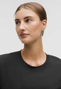 Sort T-shirt med rund halsudskæring og et struktureret stof. Nærbillede af kraven, glat hud og naturlig makeup. Håret samlet tilbage.
