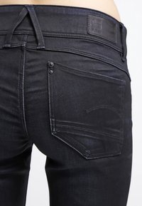 Svarta jeans i denim med slim fit, med en patch-logotyp bak, två bakfickor och en knappdetalj vid midjan.