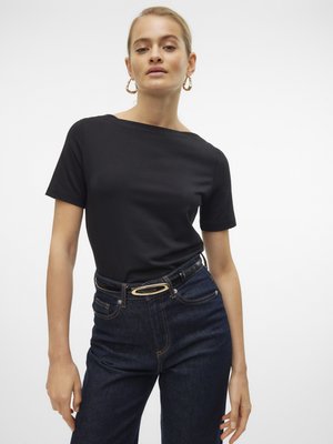 Zwart T-shirt met korte mouwen en een bootnek, gecombineerd met hoge taille donkere spijkerbroek met een gouden ovale ceintuurgesp en stikselaccenten.