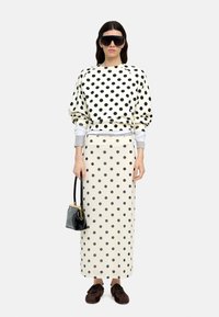 Bluzka z kropkami w kolorze kremowym z czarnymi kropkami, zestawiona z pasującą spódnicą. Dodatki to mała czarna torebka i ciemnobrązowe buty.
