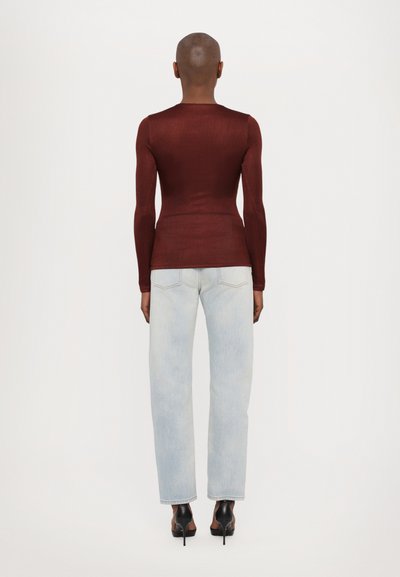 Taillierter burgunderfarbener Langarmshirt mit rundem Halsausschnitt, kombiniert mit hellblauen geraden Jeans und schwarzen High Heels. Einheitlicher Hintergrund.