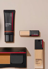 Collezione trucco Shiseido con un tubo nero, due flaconi di fondotinta nelle tonalità beige e un compatto nero con due polveri, accentuato in rosso.