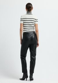 Wit en zwart gestreepte korte mouwen top gecombineerd met zwarte faux leren high-waisted broek en zwarte puntige enkelbooties.