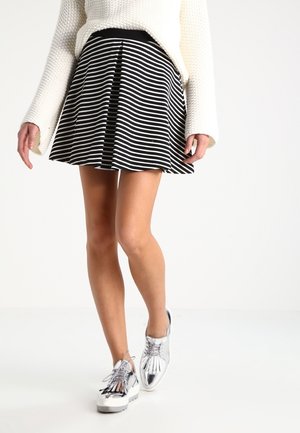 Woman walking in black and white striped skirt, cream knit sweater, and shiny silver platform lace-up shoes on white background.