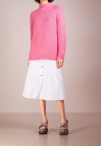 Różowy sweter z prążkowanej dzianiny z wysokim kołnierzem, w połączeniu z białą spódnicą zapinaną na guziki i kwiatowymi sandałami na platformie z teksturową podeszwą.