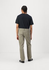 Svart kortärmad t-shirt, ljus olivgrön vida byxor, båda i bomull. Byxorna har två bakfickor; bärs med svarta sandaler.