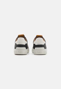 Fekete bőr sneaker cipők fehér gumitalppal, kontrasztos barna részletekkel és textúrázott hátsó saroktáblával. Az sarokra "1973 óta" van gravírozva.
