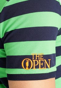 Grön och marinrandig polo t-shirt med texturerad tyg, med en broderad orange logga av "THE OPEN" på ärmen.