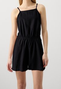 Mono negro sin mangas con escote cuadrado, cintura elástica y corte relajado. Fabricado con una tela suave y ligera de textura suave.