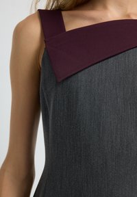 Graues Kleid mit breitem bordeauxfarbenem Schultergurt und eckigem Ausschnitt. Glatter Stoff mit taillierter Passform. Auffälliger Farbkontrast.