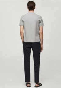 T-shirt grigia a maniche corte in cotone a costine, con vestibilità dritta, abbinata a pantaloni neri slim-fit e sandali neri.