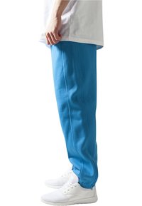Pantaloni de trening blue dintr-un material moale, cu croi slim și detalii de coasere vizibile, asortați cu adidași albi.