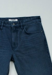 Temno modri kavbojke s ravnim krojem, opremljene z prednjim zadrgo, gumbom in dvema žepoma. Oznaka pravi "Salsa Jeans."