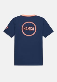 Camiseta de fútbol azul marino con un logo redondo en color coral "BARÇA" centrado en la parte posterior, con un collar coral y mangas cortas. Textura suave.