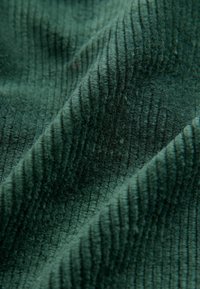 Zöld corduroy szövet bordázott textúrával, puha tapintással és finom fénylő felülettel, mély barázdákkal, amelyek hullámos mintát alkotnak.