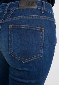 Vaqueros de mezclilla azul oscuro con una textura suave, que cuentan con un solo bolsillo trasero con costura amarilla y una etiqueta de cuero negro etiquetada "CLOSED."