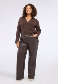 Top a maglia marrone con scollo a V e maniche lunghe abbinato a pantaloni larghi in ecopelle marrone a vita alta. Texture liscia; design elegante.