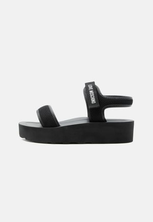 Sort plateau sandal med to mesh-remme, en over tæerne og en omkring anklen med teksten "LOVE MOSCHINO" på siden.