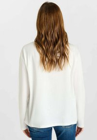 Witte blouse met lange mouwen, een gladde textuur en een afgeronde onderrand, gecombineerd met blauwe jeans. Heeft een ontspannen pasvorm en een eenvoudig ontwerp.
