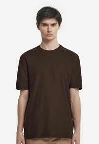 Brązowy T-shirt z krótkim rękawem wykonany z miękkiej tkaniny, z okrągłym dekoltem i luźnym krojem, charakteryzujący się gładką fakturą i minimalistycznym wzornictwem.