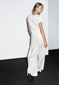 Wit T-shirt met korte mouwen, gecombineerd met losse, lichtbeige linnen broeken. De outfit heeft een eenvoudig ontwerp en een zachte textuur.