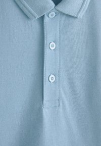 Világoskék galléros póló eleje, rajta gallér és három fehér gomb függőleges elrendezésben, struktúrált anyagon.