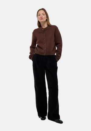 Cardigan en laine marron avec un col rond et des boutons, associé à un pantalon large noir. La texture est douce et la tenue a une coupe décontractée.