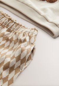 Kermansävyinen collegepaita, jossa resoroitu helma, yhdistetty beigeihin ja valkoisiin, timantinmuotoiseen kuosiin teksturoidusta kankaasta valmistettuihin shortseihin, jotka on varustettu joustavalla vyötärönauhalla.