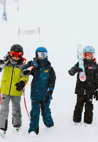 Tres niños con equipo de esquí están en una nevada. Colores: verde lima, azul marino y negro. Materiales: chaquetas aislantes, gafas y bastones de esquí.