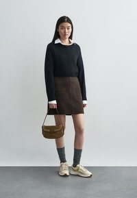 Pulover negru tricotat, cămașă albă cu guler, fustă maro cu buzunare, șosete gri, adidași crem și o geantă maro cu ținte.