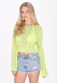 Neon zöld, rövid fazonú pulóver, chevron mintával és hosszú ujjakkal, koptatott farmertortával párosítva. Puha, könnyű kötött anyag.