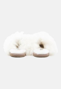 Par hvite, fluffy tøfler med brune såler sett bakfra på en plain hvit bakgrunn.
