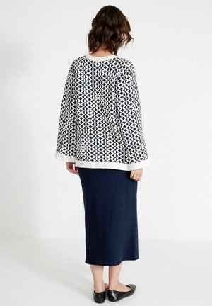 Black and white patterned sweater with wide sleeves, worn over a knee-length navy skirt. The texture appears soft with a smooth finish.