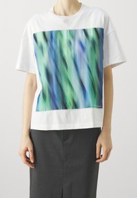 Camiseta de algodón blanca con un gran patrón gráfico abstracto en azul y verde, que presenta un corte relajado y mangas cortas. Textura suave.