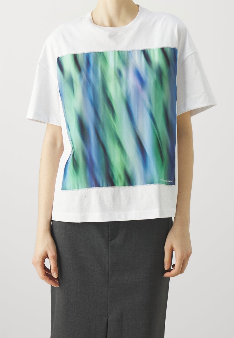 Camiseta de algodón blanca con un gran patrón gráfico abstracto en azul y verde, que presenta un corte relajado y mangas cortas. Textura suave.