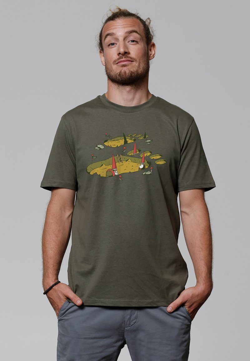 Olijfgroen katoenen t-shirt met een speelse afbeelding van kabouters, een ladder en kleurrijke elementen op een zandkleurige achtergrond.