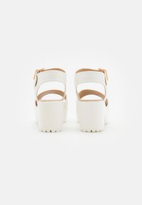 White platform sandals with adjustable ankle straps and textured white soles. Includes brown accents on the insole.