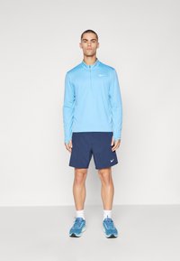 Lyseblå langærmet sportstop med en lynlås krave, marineblå shorts og blå sportssko, med Nike-logoer på toppen og shortsene.