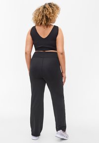 Black athletic crop top with a V-neck and black high-waisted pants. The fabric appears smooth, fitted, and stretchy. White sneakers complete the look.