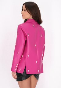 Blazer in finta pelle fucsia con dettagli in perle, colletto a punte, maniche lunghe e design con schiena spaccata. Abbinato a una mini gonna in pelle nera.