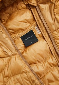 Gouden pufferjack aan de binnenkant met een geëxtrudeerd textuur, ritssluiting en zwart maatlabel. Glad stof met een lichte glans.