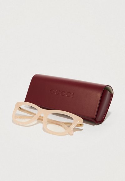 Óculos de sol Gucci com uma armação rosa claro, apresentando um formato retangular e lentes transparentes, colocados ao lado de um estojo macio bordeaux gravado com "GUCCI."