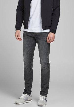 Donkergrijze jeans met een slim fit en subtiele vervaging. Gecombineerd met een wit t-shirt en een zwarte ritsjack. Schoenen zijn lichtgrijs met marineblauwe accenten.
