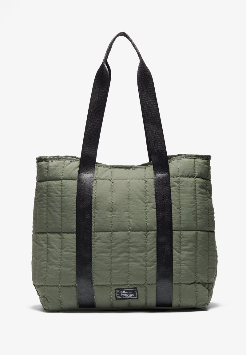 Quilted olivengrønn totebag med svarte stoffhåndtak, rektangulær form og merket detalj i bunnen. Myk tekstur med sydd mønster.