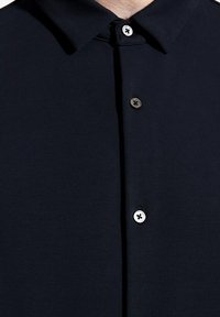 Camisa azul marino con cuello clásico, que presenta cuatro botones en la parte delantera y una tela suave y texturizada. Diseño simple y estructurado.