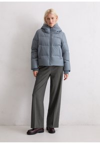 Helle blaue Daunenjacke mit Kapuze, ausgestattet mit gestepptem Futter und einem Reißverschluss auf der Vorderseite. Kombination mit grauen weit geschnittenen Hosen und dunklen Schuhen.